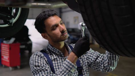 Indian Car Mechanic Man Working Under Lifted Car In Auto Repair Service