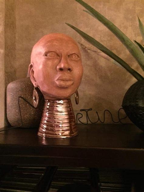 A Sculpture Of A Man S Head On A Table Next To A Potted Plant