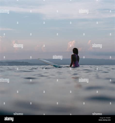 Silhouette Of Female Surfer Sitting On Surfboard In Ocean At Sunset