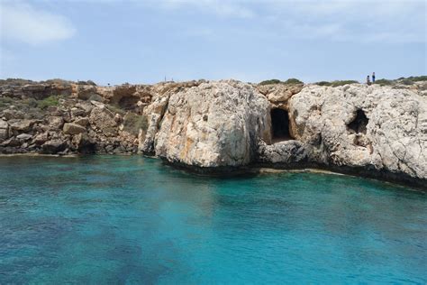 two people standing on the edge of a rock outcropping over blue water