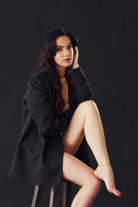 Sexy Brunette With Curly Hair In Luxury Clothes Sits On Chair In The Studio Against Black