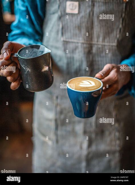 Barista With Apron Pouring Steamed Milk Into Coffee Cup Making A Flat