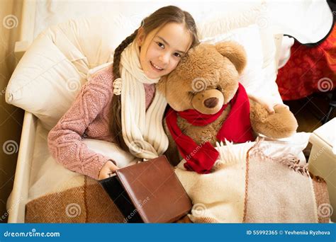 Cute Smiling Girl Reading Book With Teddy Bear In Bed Stock Image