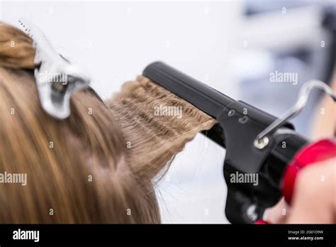 Female Hairdresser Curling Hair Of Client In Beauty Salon Closeup