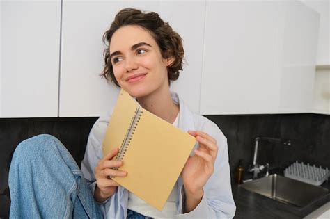 Portrait De Jeune Femme Moderne Assise Dans La Cuisine Feuilletant Des