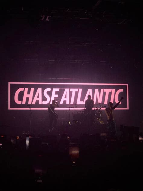 The Band Chase Atlantic On Stage In Front Of A Neon Sign