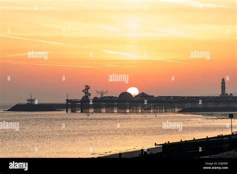 The Sun Rising Into An Orange Sky Over The Silhouette Of The Pier At