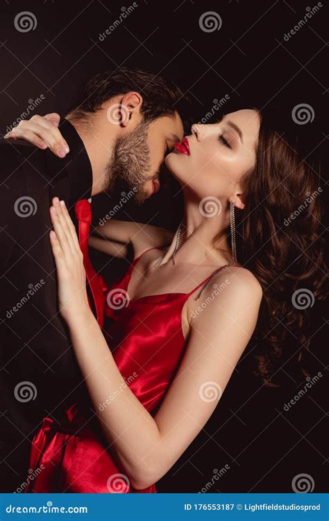 Side View Of Man In Suit Kissing Attractive Woman In Red Dress Stock