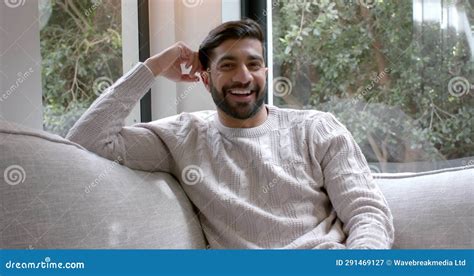 Portrait Of Happy Biracial Man Sitting On Sofa Smiling At Home Slow