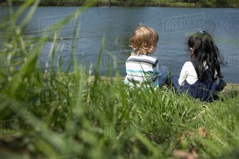 Children Sitting On Riverbank Together Stock Photo Dissolve