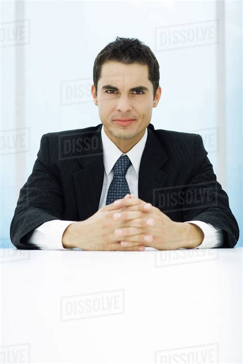 Businessman Sitting At Table With Hands Clasped Looking At Camera