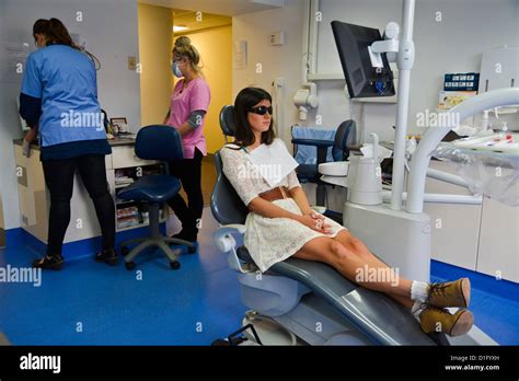 Young Woman Waiting In Dentists Chair While The Dentist And Assistant