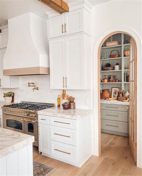 A Kitchen With White Cabinets And An Arched Doorway Leading To The