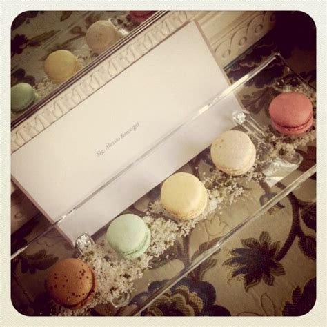 An Assortment Of Macaroons In A Clear Box On A Floral Tableclothed Surface