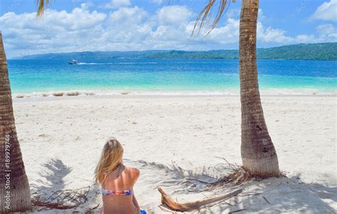 Frau sitzt im Bikini auf Handtuch mit dem Rücken zur Kamera am weißen