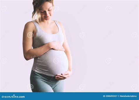 Beautiful Young Pregnant Woman In Good Fit Holds Hands On Her Belly