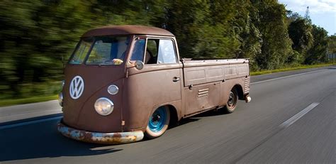 An Old Vw Bus Is Driving Down The Road With Trees In The Back Ground