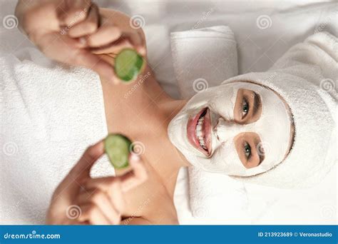 Spa Beautiful Woman With A Clay Mask On Her Face And Cucumbers In