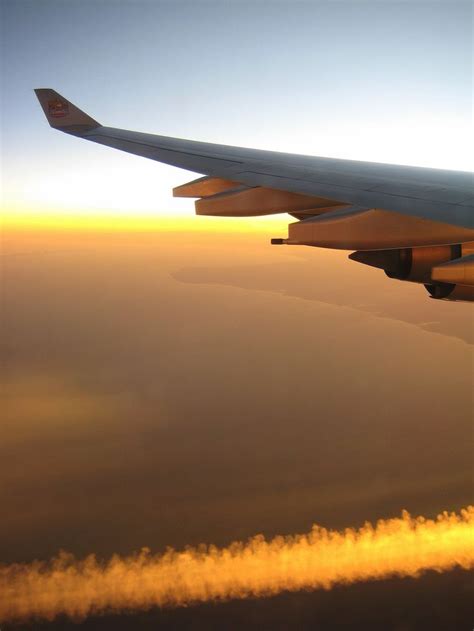 The Wing Of An Airplane As It Flies Through The Sky With Clouds In The