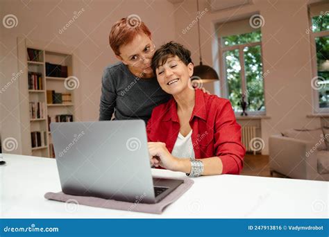 Mature Lesbian Couple Smiling And Hugging While Using Laptop Stock