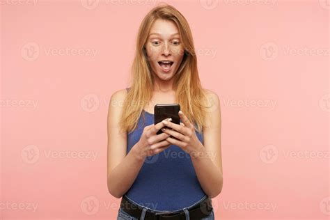 Suprised Young Pretty Long Haired Redhead Woman In Blue Shirt Looking Excitedly On Screen Of Her