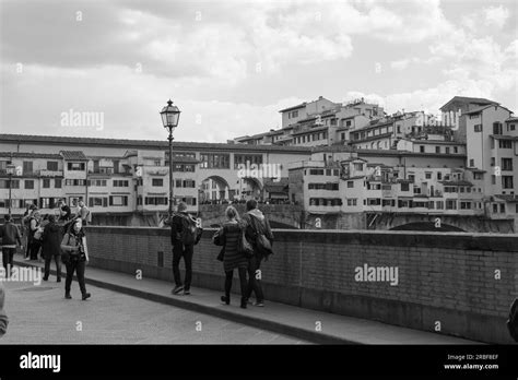 Tourists Strolling Along The Arno River And View Of The Crowded Ponte