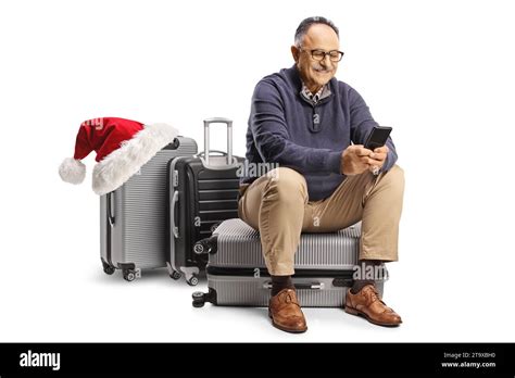 Mature Man Sitting On A Suitcase With A Santa Claus Hat And Using A