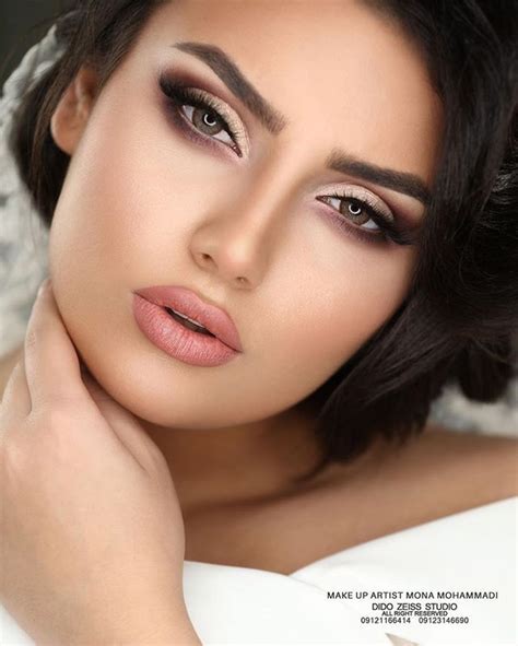 A Woman With Dark Hair And Makeup Looks At The Camera While Holding Her