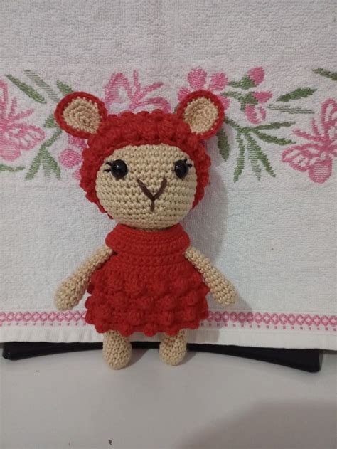 A Small Crocheted Teddy Bear In A Red Dress Sitting On A White Towel