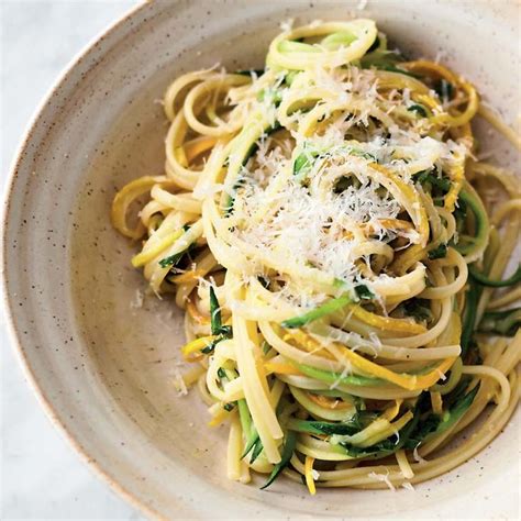 A White Bowl Filled With Pasta Covered In Parmesan Cheese And Spinach