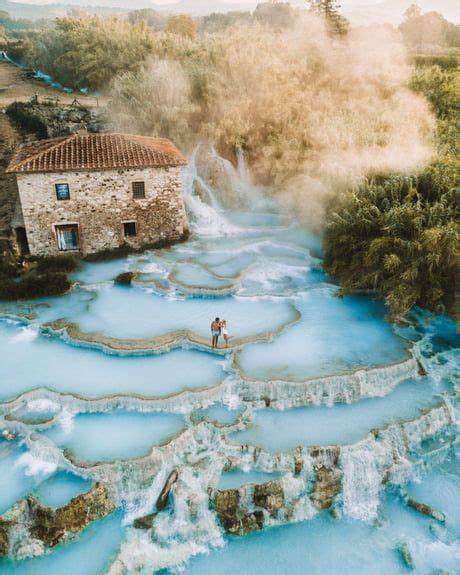 A Man Standing On The Edge Of A River Next To A Stone Building And