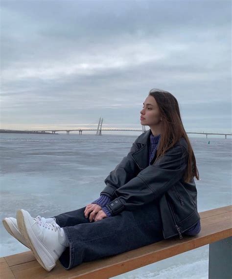 A Woman Sitting On Top Of A Wooden Bench Next To The Ocean Under A