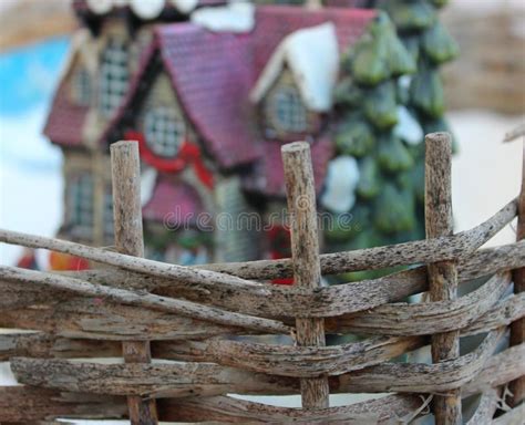 Defocused Toy Christmas House Behind Wicker Fence Made From Wooden