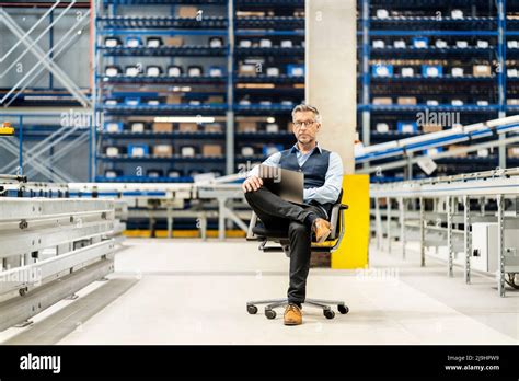 Mature Businessman With Laptop Sitting On Chair In Warehouse Stock Photo Alamy