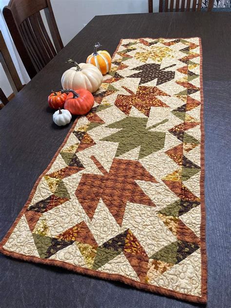 A Quilted Table Runner With Pumpkins And Gourds On The Table Top