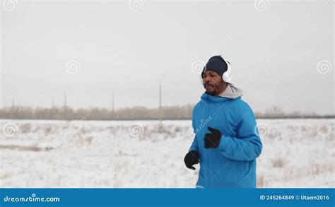 Black Man In Headphones And Warm Winter Clothes Is Jogging Outdoors