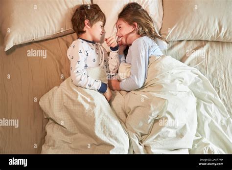 Brother And Sister Are Lying In Bed In The Bedroom And Silly Happily