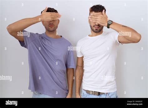 Homosexual Gay Couple Standing Over White Background Covering Eyes With Hand Looking Serious