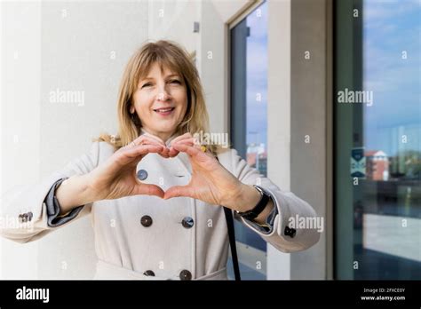 Mature Woman Gesturing Heart Shape Sign By Building Stock Photo Alamy