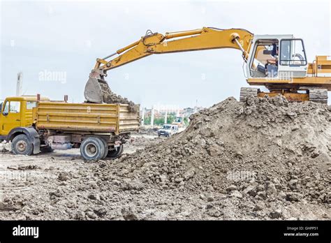 Yellow Excavator Is Filling A Dump Truck With Soil At Construction Site