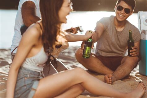 Amigos Novos Que Bebem A Cerveja Ao Sentar Se Junto Na Praia Imagem De