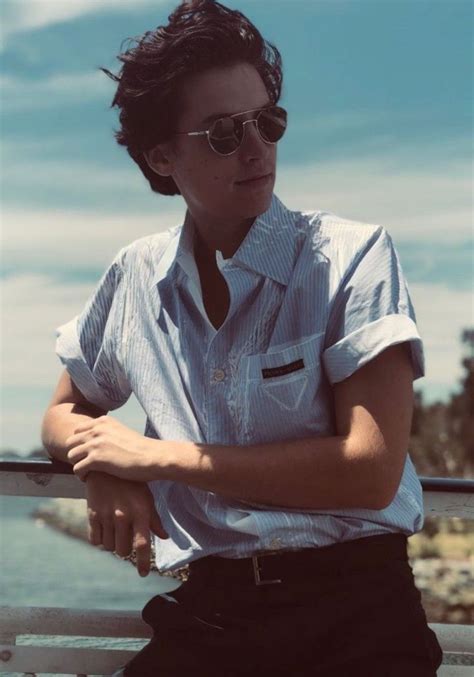 A Man In Sunglasses Leaning On A Rail Near The Water With His Arms