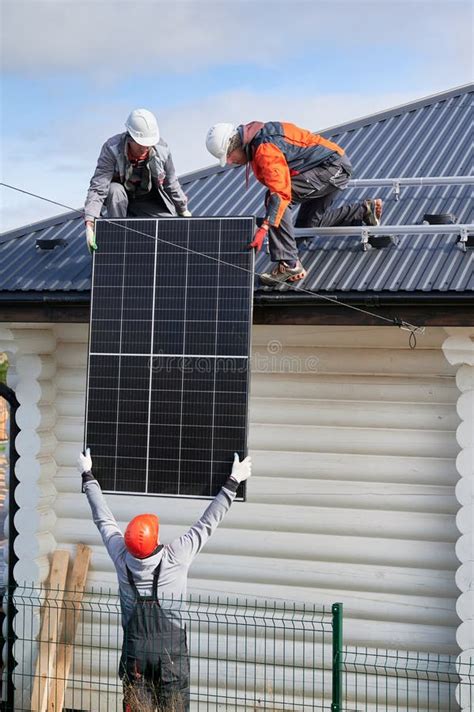 Professional Technicians Lifting Solar Panels On A Roof Of House Stock