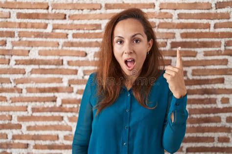 Brunette Woman Standing Over Bricks Wall Pointing Finger Up With Successful Idea Stock Image