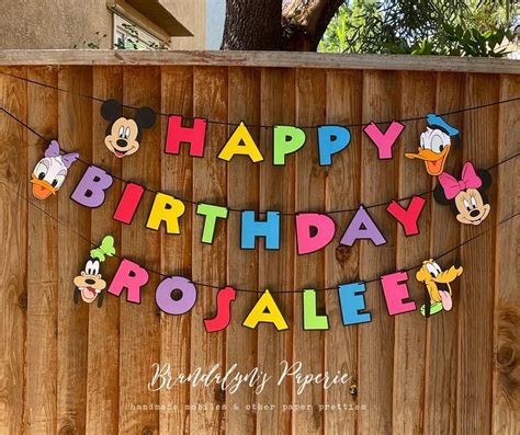 A Happy Birthday Rosalee Banner With Mickey Mouse Cutouts Hanging On A Fence