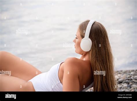 A Woman Wearing Headphones And A White Bikini Is Laying On The Beach Stock Photo Alamy