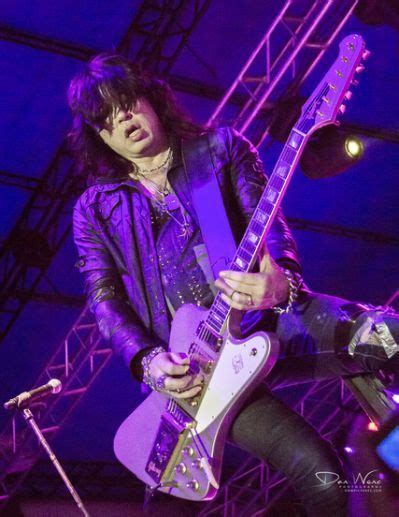 A Man Playing Guitar On Stage With Purple Lighting Behind Him And His Legs In The Air