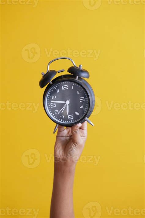 Person Hand Holding Alarm Clock On Yellow Background Stock