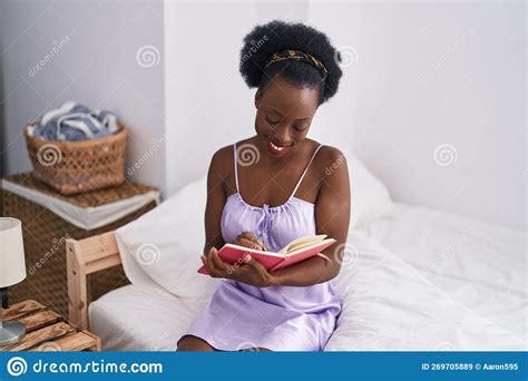 African American Woman Reading Book Sitting On Bed At Bedroom Stock