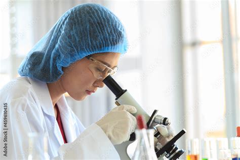 Asian Female Professional Scientist In White Lab Coat Safety Glasses Hygiene Cap And Rubber